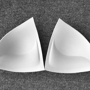 Könnte beinhalten: Zwei weiße, dreieckige BH-Körbchen. Die Körbchen bestehen aus einem weichen, flexiblen Material und haben eine glatte, nahtlose Oberfläche.