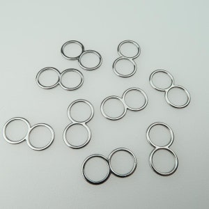 May include: A collection of silver-colored metal infinity connectors, each composed of two connected circles. The connectors are arranged on a white surface, with varying orientations. These jewelry findings are suitable for crafting.