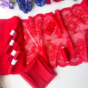May include: A collection of red sewing supplies including a wide strip of floral lace trim, a folded piece of red fabric, four small rolls of red elastic ribbon, a red spool of thread, and a red bra hook and eye closure fastener.