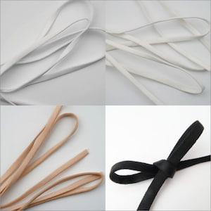May include: Four spools of ribbon in different colors and textures. The first spool is white, the second is white, the third is beige, and the fourth is black. The black ribbon is tied in a bow.