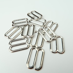 May include: A pile of silver metal slider buckles, also known as D-rings, used for adjusting straps on clothing or bags.