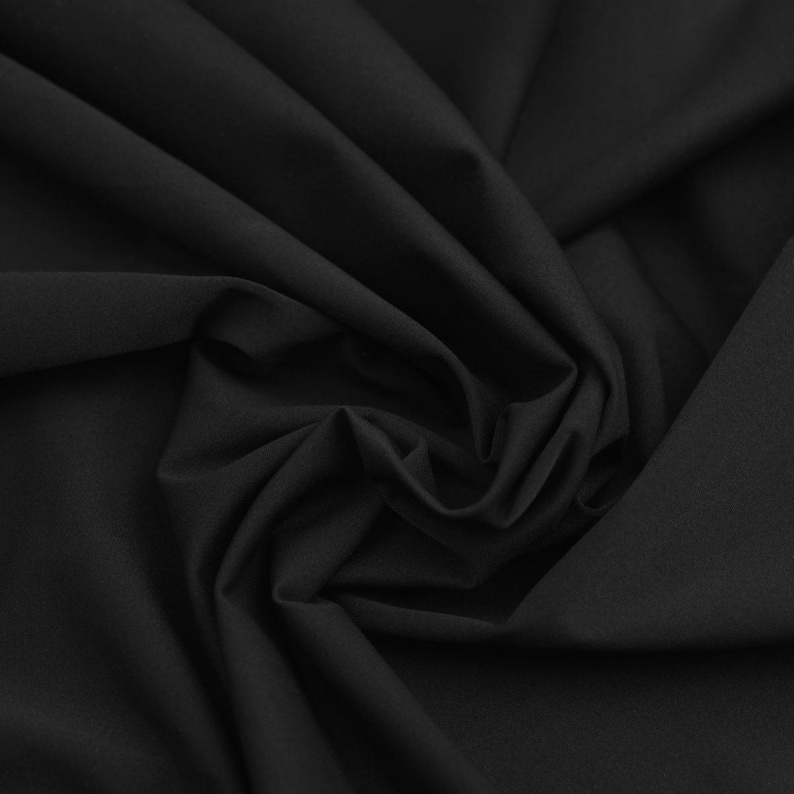 May include: Close-up of black fabric with visible folds and soft texture. The fabric appears to be a solid color, with no visible patterns or designs. The lighting creates shadows that emphasize the folds and texture of the material.