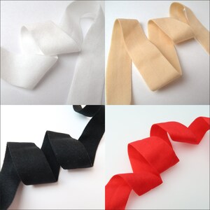 May include: Four rolls of fabric ribbon in different colors: white, beige, black, and red. The ribbon is folded and arranged in a decorative pattern.