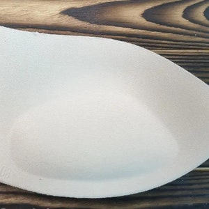 May include: A beige foam bra cup with a rounded shape and a smooth texture. The cup has a size label that reads "7.05".