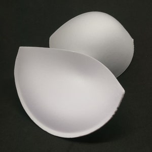 May include: Two white foam bra inserts, shaped like half circles, designed to add volume to a bra cup.