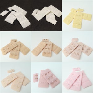 May include: Set of bra extenders in five colors: white, beige, light pink, yellow, and pink. Each extender has three rows of hooks and eyes.