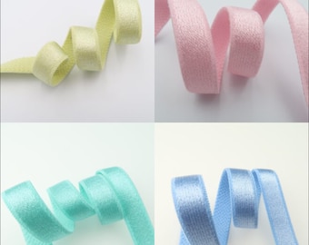 May include: Four spools of elastic ribbon in different pastel colors: light green, pink, light blue, and blue. The ribbon is soft and has a subtle sheen.