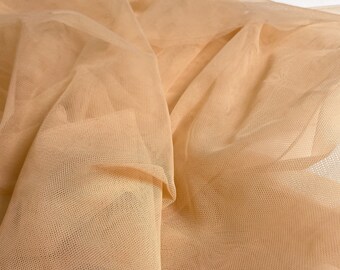 May include: A close-up of a piece of beige tulle fabric. The fabric is soft and delicate, with a fine mesh weave.