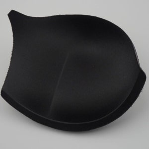 May include: Black bra cup padding insert. The padding is made of a soft, flexible material and has a smooth, rounded shape.