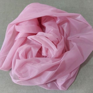 May include: A pink sheer fabric, folded and bunched up, creating a soft and delicate texture.