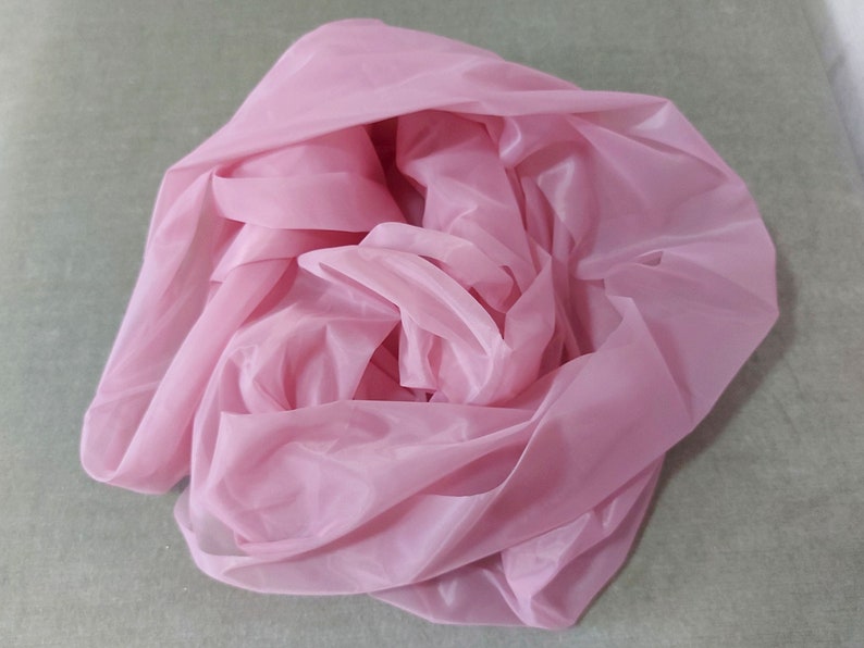 May include: A pink sheer fabric, folded and bunched up, creating a soft and delicate texture.