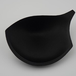 May include: Black bra cup insert made of foam. The insert is shaped like a half-circle with a pointed tip.