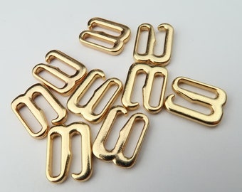 May include: A group of gold-coloured metal bra strap adjusters. The adjusters are in various positions, showing the different ways they can be used.