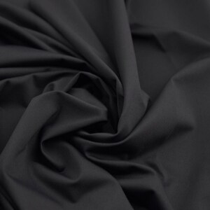 May include: A close-up shot of a dark gray fabric with a smooth texture. The fabric is draped and swirled, creating soft folds and shadows. The material appears to be a solid color, with no visible patterns or designs.