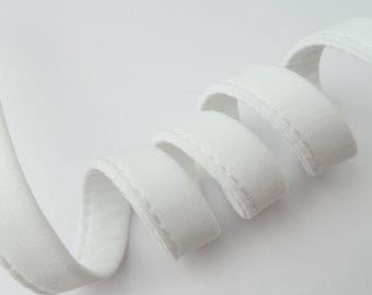 Può includere: Nastro di sbieco bianco con un bordo cucito. Il nastro è piegato e arrotolato a forma di spirale.