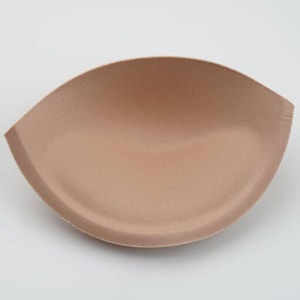 May include: A pair of beige bra inserts made of soft foam. The inserts are shaped like half circles and have a smooth, seamless finish.