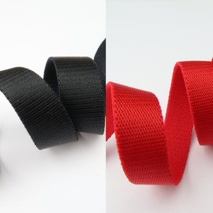 May include: Two spools of woven nylon webbing, one black and one red. The webbing is approximately 1 inch wide.