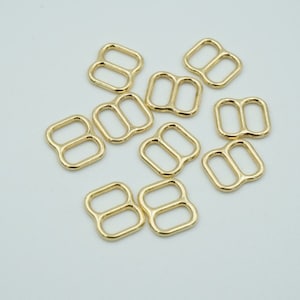 May include: Ten gold-toned metal slider buckles. The buckles are rectangular with two oval-shaped holes.