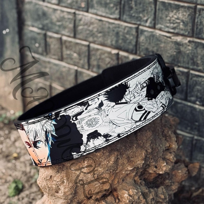 May include: Black weightlifting belt with a white and black anime print. The belt has a black buckle and stitching.