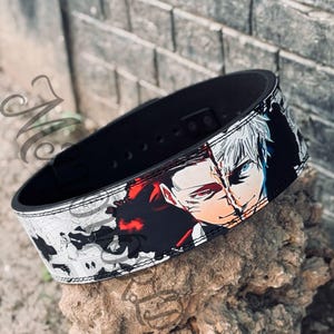 May include: Black weightlifting belt with a white and black anime-style graphic of two characters with red and blue accents. The belt has a stitched edge.