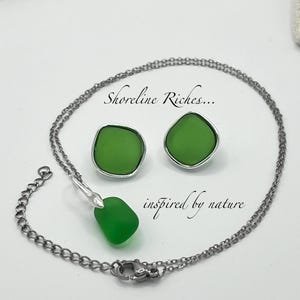 May include: A jewelry set featuring a necklace and matching earrings. The set includes a silver-toned chain necklace with a green pendant and a pair of green stud earrings. The text "Shoreline Riches... inspired by nature" is also visible.