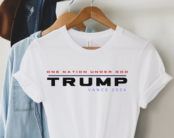 Könnte beinhalten: Weißes T-Shirt mit dem Aufdruck "ONE NATION UNDER GOD TRUMP VANCE 2024". Der Text ist in Rot, Blau und Schwarz.