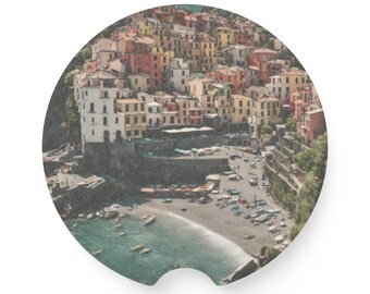 May include: A colorful cityscape with buildings clustered together on a hillside overlooking a blue ocean with boats. The buildings are a mix of yellow, orange, red, and white.