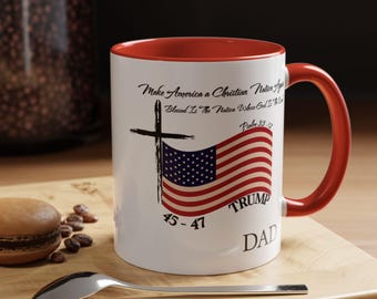 Könnte beinhalten: Weißer Keramikbecher mit roter Innenseite und Henkel. Der Becher zeigt ein Kreuz, ein amerikanisches Flaggen-Design und den Text "Make America a Christian Nation", "TRUMP" und "DAD".