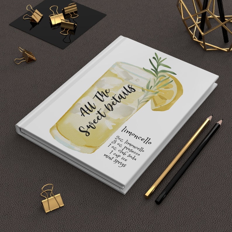 Op de afbeelding: Een wit notitieboekje met de tekst "All The Sweet Details" en een aquarel-illustratie van een glas limoncello met een citroenschijfje en een rozemarijntak. Het recept voor limoncello staat onder de illustratie: 2 oz limoncello, 3 oz prosecco, 1 oz club soda, 1 kopje ijs, muntblaadjes.