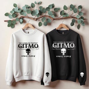 May include: Two sweatshirts, one white and one black, with a graphic print of a skull and barbed wire. The text "WHAT STORM MR PRESIDENT? GITMO" is printed on both sweatshirts. The coordinates "19.5403 N-75-0554 W" are printed below the graphic on the white sweatshirt and "19.5403 N-75-0551 W" are printed below the graphic on the black sweatshirt.