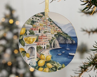 May include: A round, colorful Christmas ornament featuring a watercolor painting of a coastal town with a lemon tree in the foreground. The town is built on a hillside overlooking a blue ocean with boats.