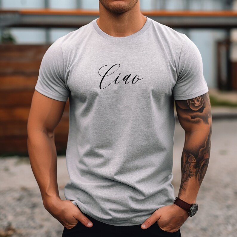 May include: A light grey t-shirt featuring the word "Ciao" in black cursive script. The short-sleeved shirt is made of a soft material and has a crew neck. The t-shirt is a casual wear item.