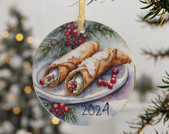 May include: Round Christmas ornament with a watercolor painting of two cannoli pastries on a white plate with red berries and green pine sprigs. The year 2024 is written in black script at the bottom of the ornament.