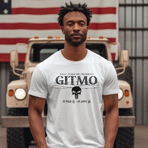 May include: White t-shirt with a black graphic print of a skull with barbed wire and the text "WHAT STORM MR PRESIDENT? GITMO 17.5463 N -75.0554 W"