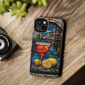 May include: A stained glass phone case with a glass of orange juice, lemons, and a view of a town in the background.