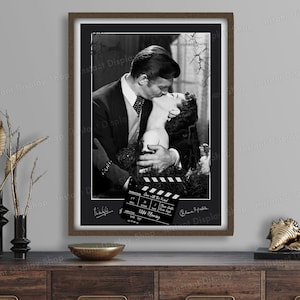 Peut inclure: Photographie encadrée en noir et blanc d'une scène romantique du film "Autant en emporte le vent". L'image montre un homme embrassant une femme, avec un clap de cinéma au premier plan. Le cadre est marron.