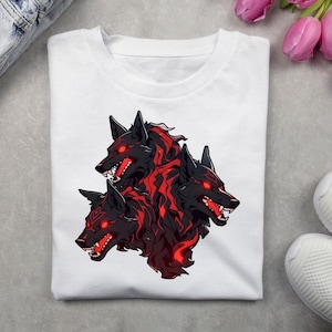 Puede incluir: Camiseta blanca con un estampado gráfico de tres lobos negros con ojos rojos brillantes y llamas. Los lobos están mirando hacia adelante con la boca abierta.