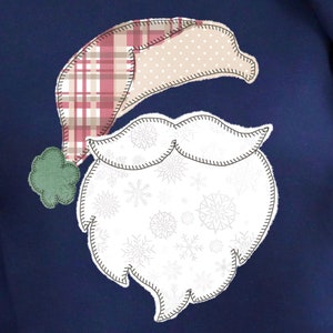 May include: A navy blue sweatshirt with a white and red patchwork Santa Claus design. The Santa Claus design has a white beard with snowflakes and a red and white plaid hat.