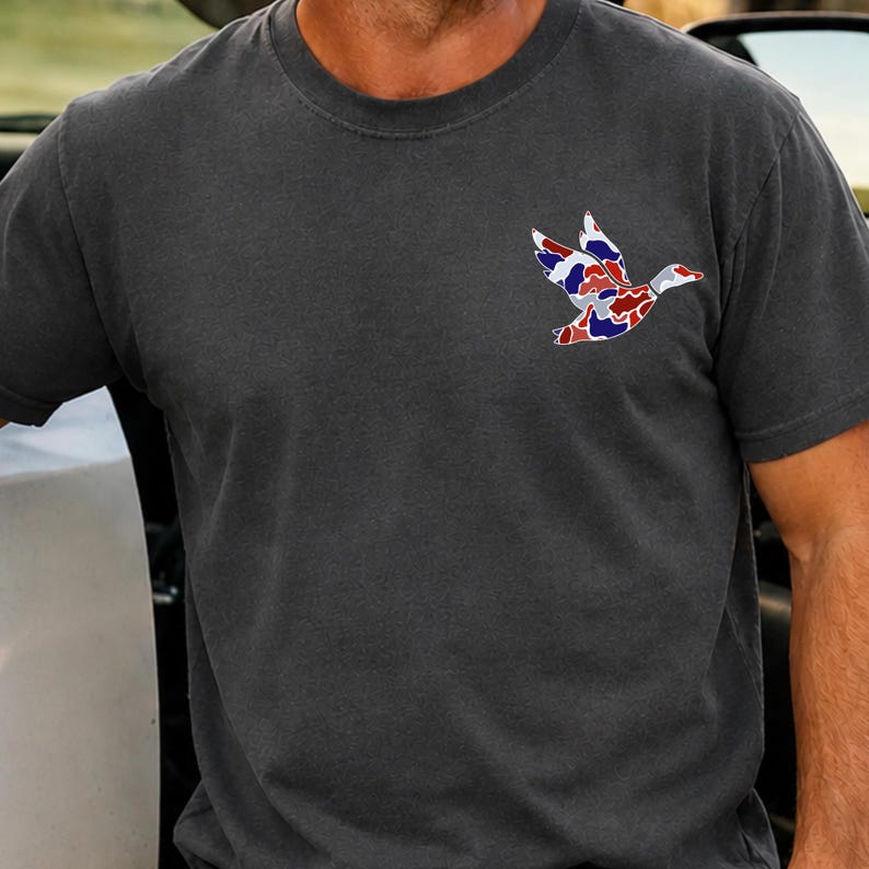 K&ouml;nnte beinhalten: Dunkelgraues T-Shirt mit einem bunten Entenmuster auf der Brust. Das Entenmuster besteht aus roten, wei&szlig;en und blauen Mustern. Das T-Shirt hat einen Rundhalsausschnitt und kurze &Auml;rmel.