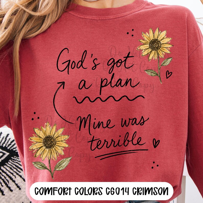 Puede incluir: Una sudadera de cuello redondo color carmes&iacute; con el texto impreso en negro God's got a plan, Mine was terrible, acompa&ntilde;ada de dos girasoles amarillos con tallos y hojas verdes, peque&ntilde;os corazones negros y puntos, con el texto COMFORT COLORS C6014 CRIMSON.