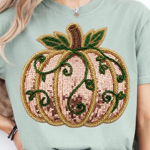 Op de afbeelding: Lichtgroen T-shirt met een gedetailleerd pompoenontwerp. De pompoen is gemaakt van pailletten en heeft goudkleurige randen, groene bladeren en ranken. Het ontwerp is gecentreerd op de voorkant van het shirt.