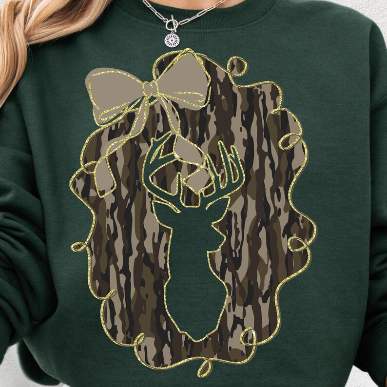 Puede incluir: Una sudadera verde oscuro con la silueta de una cabeza de ciervo dentro de una corona de camuflaje. La corona tiene un contorno dorado brillante y un lazo. Un estilo c&oacute;modo e informal.