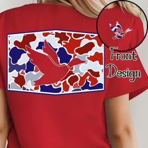 K&ouml;nnte beinhalten: Rotes T-Shirt mit einem gro&szlig;en rechteckigen Design auf dem R&uuml;cken, das eine rote Entensilhouette &uuml;ber einem Camouflagemuster in Rot, Wei&szlig; und Blau zeigt. Eine kleinere Version des Enten-Designs befindet sich auf dem rechten oberen &Auml;rmel. Die Worte "Front Design" sind ebenfalls sichtbar.