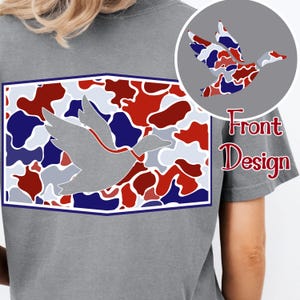 K&ouml;nnte beinhalten: Graues T-Shirt mit einem Enten-Design. Das Design zeigt eine graue Entensilhouette mit einem roten Band, vor einem rot, wei&szlig; und blau getarnten Muster in einem wei&szlig; und blau umrandeten Rechteck. Die Worte "Front Design" sind ebenfalls sichtbar.