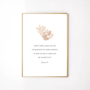 Op de afbeelding: Een ingelijste print met een gouden rand toont een aquarel illustratie van een beige blad en tekst. De tekst luidt: "WAT ZULLEN WIJ DAN OVER DEZE DINGEN ZEGGEN? ALS GOD VOOR ONS IS, WIE ZAL TEGEN ONS ZIJN?" Romeinen 8:31.