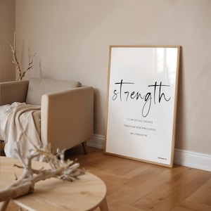 Op de afbeelding: Een ingelijste print met het woord "strength" in elegant zwart schrift. Daaronder staat de tekst "Ik kan alles doen door Hem die mij kracht geeft." De print heeft een licht houten frame en wordt weergegeven in een kamer met neutrale tinten.