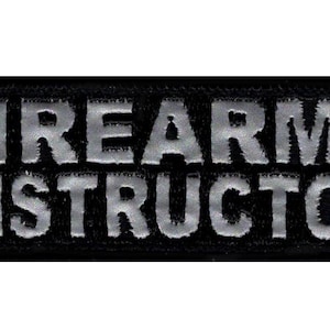 Könnte beinhalten: Schwarzer Patch mit den Worten "FIREARMS INSTRUCTOR" in silberner Stickerei.