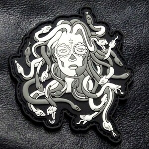 May include: A black and white embroidered patch of a woman's face with snakes for hair. The woman's face has a sugar skull design.