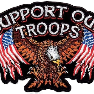 Pode incluir: Etiqueta bordada com uma águia careca com as asas abertas segurando uma bandeira americana em cada garra. A águia está centrada sob o texto "SUPPORT OUR TROOPS" com uma estrela de cada lado.