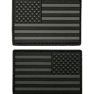 May include: Two black and gray American flag patches. The patches are made of a textured material and have a stitched border.